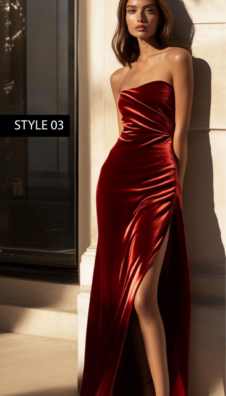 May include: A long, red velvet dress with a single slit on the left side. The dress has a strapless neckline and a fitted bodice. The dress is styled with a simple, elegant look.