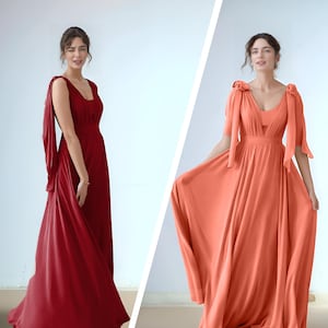 May include: Two women wearing long, flowing maxi dresses. The dress on the left is a deep red color, while the dress on the right is a coral color. Both dresses have a V-neckline and a fitted bodice.