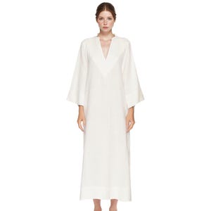 May include: A long, white dress with a V-neckline and wide sleeves. The dress is floor-length and appears to be made of a lightweight fabric. The sleeves are wide and end at the mid-forearm. The dress has a simple, elegant design.