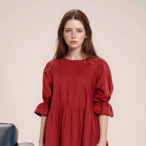 May include: A woman wearing a red, long-sleeved dress with a round neckline and a gathered skirt.