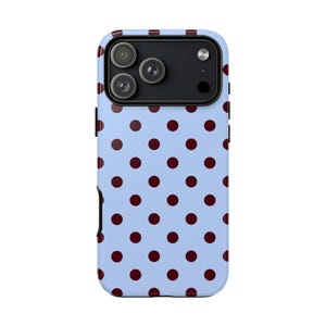 May include: A light blue phone case featuring a repeating pattern of dark red polka dots. The case has a black camera module with three lenses. The case is designed to fit a smartphone.