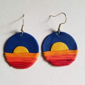May include: A pair of blue, yellow, orange, and red sunset earrings. The earrings are made of polymer clay and have a simple oval shape.