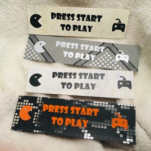 May include: Four bookmarks with a black and white pixelated design. Each bookmark has a black and white video game controller icon and the text "PRESS START TO PLAY".