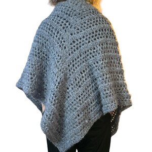 May include: A gray crocheted poncho with a lacy pattern. The poncho is worn by a person with long, curly hair.