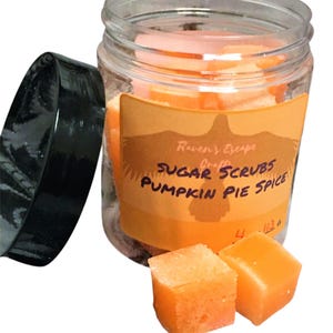 May include: A clear glass jar filled with orange sugar scrub cubes. The jar has a black lid and a label that reads "Raven's Escape Crafts Sugar Scrubs Pumpkin Pie Spice".