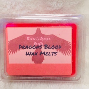 Peut inclure: Un fondant de cire rouge dans un récipient en plastique transparent avec une étiquette qui dit "Raven's Escape Crafts Dragons Blood Wax Melts". L'étiquette présente une silhouette de corbeau avec ses ailes déployées.