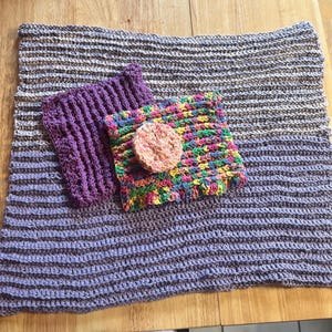 May include: Three crocheted dishcloths, one purple, one multicolored, and one gray and white, with a round, natural sponge in the center.