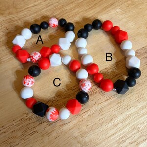 May include: Three silicone bracelets with red, white, and black beads. The bracelets are labeled A, B, and C.