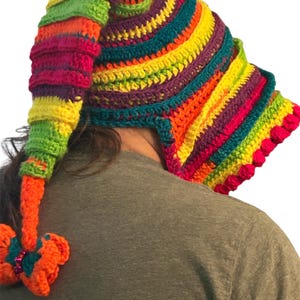 May include: A colorful, handmade crochet hat with a long, pointed tip and ear flaps. The hat features a vibrant rainbow of colors, including red, orange, yellow, green, and purple. The hat has a decorative orange flower with teal accents.