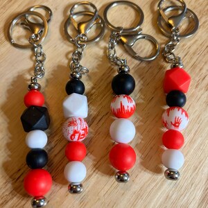 May include: Four keychains with different red, white, and black bead designs. Each keychain has a silver metal ring and chain.
