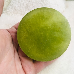 May include: A round, green soap bar with a shimmery finish.
