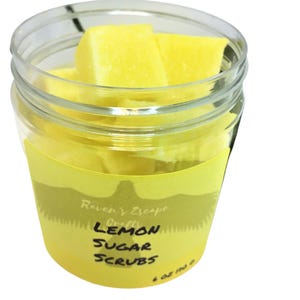 May include: A clear glass jar filled with yellow lemon sugar scrub cubes. The jar has a yellow label with the text "Raven's Escape Crafts Lemon Sugar Scrubs".