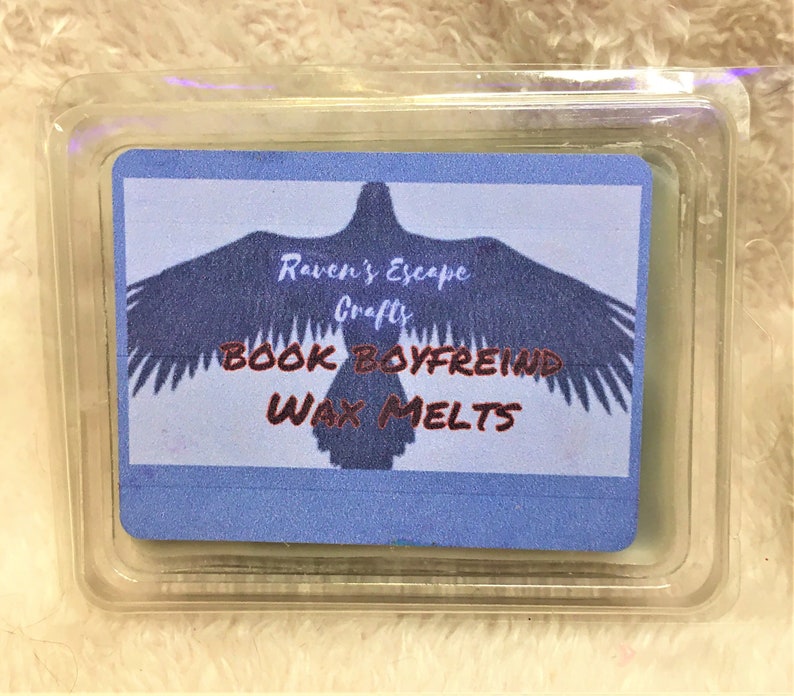 Clear plastic six part wax melt clamshell showing dark grey wax. Label has a raven across and reads Raven's Escape Crafts book boyfriend wax melts. Background is fluffy white