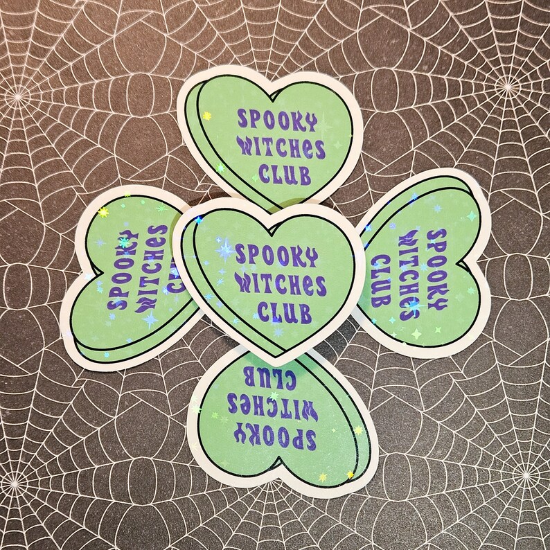 Op de afbeelding: Vier groene hartvormige stickers met de tekst "Spooky Witches Club" in paarse letters. De stickers hebben een glinsterende afwerking.