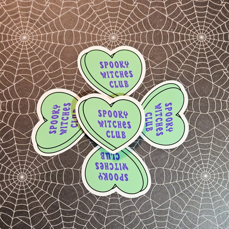 Op de afbeelding: Vier groene hartvormige stickers met de tekst "Spooky Witches Club" in witte en paarse letters.