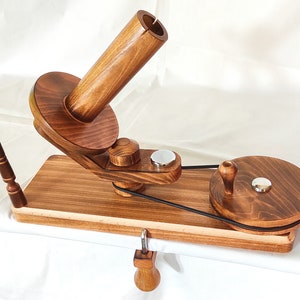 May include: Wooden yarn swift with a spindle and a clamp. The swift is made of natural wood with a dark brown stain. The spindle is made of wood and has a metal knob. The clamp is made of metal and has a wooden handle.