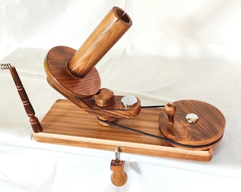 May include: Wooden yarn swift with a spindle and a clamp. The swift is made of natural wood with a dark brown stain. The spindle is made of wood and has a metal knob. The clamp is made of metal and has a wooden handle.