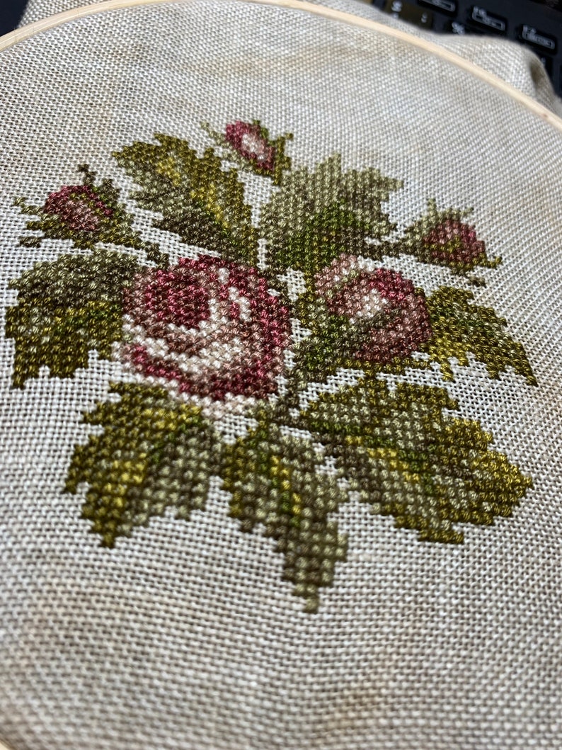 K&ouml;nnte beinhalten: Nahaufnahme einer Kreuzstich-Stickerei mit einer Gruppe von rosa und wei&szlig;en Rosen mit gr&uuml;nen Bl&auml;ttern.