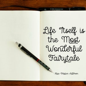 May include: A white notebook with a black pen and a quote written in black ink: "Life itself is the most wonderful fairytale." The quote is attributed to Hans Christian Andersen.