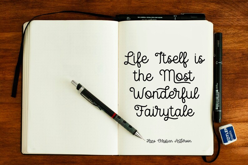 May include: A white notebook with a black pen and a quote written in black ink: "Life itself is the most wonderful fairytale." The quote is attributed to Hans Christian Andersen.