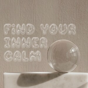 May include: A clear glass sphere sits on a white marble pedestal against a beige background. The words "FIND YOUR INNER CALM" are written in a clear, bubbly font.