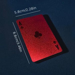 May include: A red Ace of Clubs playing card with a textured finish. The card is 8.8cm high and 5.8cm wide. The card's design includes the suit symbol and the letter 'A'. It casts a shadow on a dark blue surface.