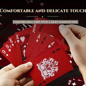 May include: A hand holding a fanned deck of red playing cards. The cards feature white suits, numbers, and face cards. The text "COMFORTABLE AND DELICATE TOUCH" and "COMFORTABLE GRIP WITH A SILKY SMOOTH FEEL" are visible.