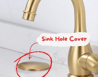 May include: A gold-colored sink hole cover is shown in the image. The cover is circular and sits on a white countertop. A gold faucet is in the background. The text "Sink Hole Cover" is in a white cloud-shaped bubble.