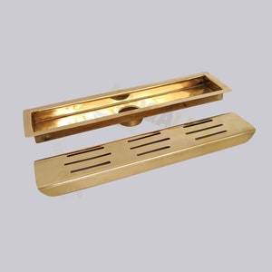 May include: A gold-colored drain grate with a rectangular frame and a slotted insert. The grate is designed for use in showers or bathrooms.