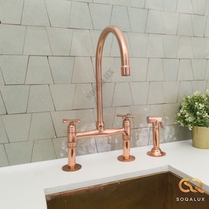 May include: A copper kitchen faucet with a high arc spout and two handles. The faucet is mounted on a white countertop with a copper sink.