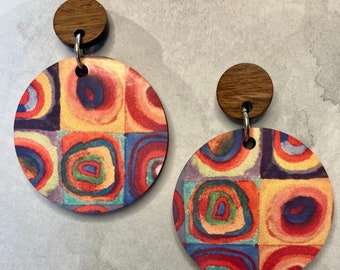 May include: A pair of colorful wooden earrings with a geometric pattern of circles and squares. The earrings are made of wood and have a silver hook.