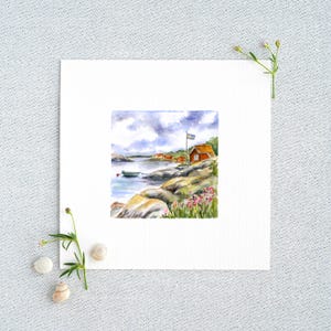 Könnte beinhalten: Ein Aquarell auf quadratischem Papier zeigt eine Küstenszene mit einer roten Holzhütte, einem kleinen grünen Boot an felsigen Ufern und einer wehenden schwedischen Flagge. Die Landschaft zeigt rosa Wildblumen im Vordergrund und einen bewölkten Himmel.