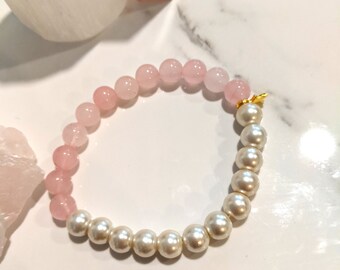 May include: A bracelet with alternating sections of pink rose quartz beads and white faux pearls. The bracelet has a gold-coloured clasp. The jewellery is displayed on a white marble surface.