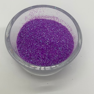 May include: A clear, round container filled with vibrant purple glitter. The glitter has a fine texture and reflects light, creating a sparkling effect. Ideal for crafts, nail art, or decorative projects.