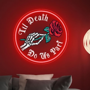 Op de afbeelding: Een neon-bord met een witte cirkel en rode omtrek. Het bord zegt "Til Death Do Us Part" in een gotisch lettertype. Een skelet hand houdt een rode roos vast met groene bladeren.
