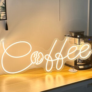 May include: White neon sign with the word "Coffee" in a cursive font. The sign includes a stylised coffee bean graphic.