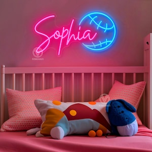 May include: A pink and blue neon sign with the name "Sophia" and a basketball. The sign is hanging on a pink wall above a white crib with pink bedding and colorful pillows.
