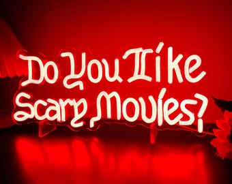 May include: A bright red neon sign featuring the white text "Do You Like Scary Movies?" in a stylised, flowing font. The sign is mounted on a clear acrylic backing and emits a vibrant red glow that illuminates the surrounding area.
