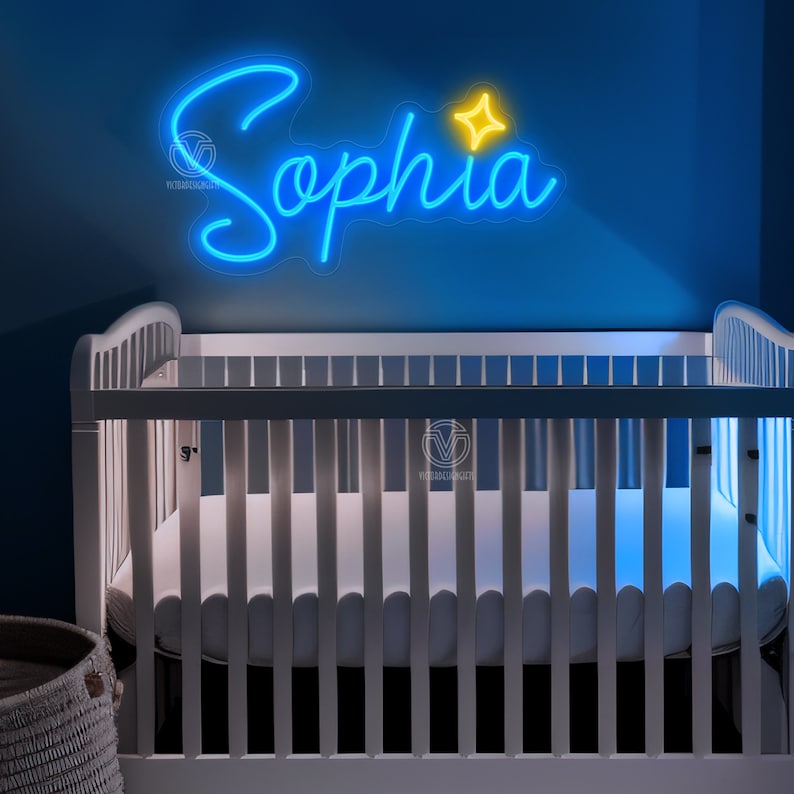 K&ouml;nnte beinhalten: Ein individuelles Neonschild mit dem Namen Sophia in leuchtend blauer Schreibschrift, erg&auml;nzt durch ein kleines gelbes vierzackiges Sternsymbol. Das Schild ist auf einer transparenten Acrylplatte montiert und h&auml;ngt &uuml;ber einem wei&szlig;en Babybett.