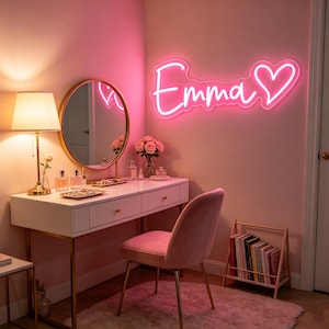 K&ouml;nnte beinhalten: Ein leuchtend pinkes Neonschild an der Wand, das den Namen Emma in Schreibschrift gefolgt von einem Herzsymbol zeigt. Das Schild strahlt ein lebendiges Leuchten aus, das die Umgebung in ein sanftes rosa Licht taucht und einen Blickfang bildet.