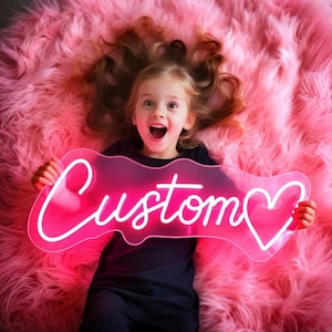 K&ouml;nnte beinhalten: Ein leuchtend pinkes Neonschild mit dem Wort Custom in Schreibschrift, gefolgt von einem Herzumriss. Das Schild besteht aus einer transparenten Acrylplatte und wird horizontal gehalten, wobei es ein lebhaftes Leuchten vor einem pinken Hintergrund erzeugt.