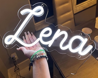 Könnte beinhalten: Ein weißes Neon-Schild mit dem Namen "Lena" in einer kursiven Schriftart. Das Schild ist auf einer durchsichtigen Acrylplatte montiert.