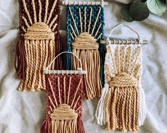 May include: Four woven wall hangings with a sun design. The hangings are made with brown, teal, white, and red yarn. Each hanging has a fringe of yarn at the bottom.