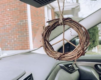May include: A brown twig wreath with a peace sign in the center hangs from the rearview mirror of a car.