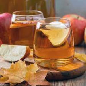 May include: Two glasses of apple cider with apple slices in them. The glasses are on a wooden surface with fall leaves and apples.