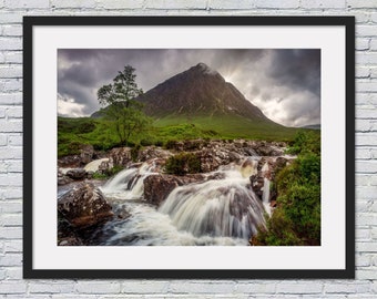 May include: A framed photograph of a waterfall cascading down a rocky hillside with a mountain in the background. The sky is cloudy and the water is flowing quickly.