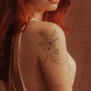 May include: A black line art tattoo design of a floral bouquet with leaves and flowers on a person's shoulder.