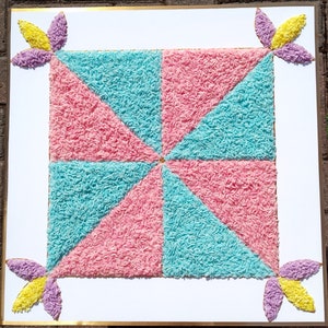 Puede incluir: Un diseño cuadrado hecho con arroz rosa y azul, con cuatro formas de flores amarillas y moradas en las esquinas.