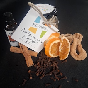 Könnte beinhalten: Eine Auswahl aromatischer Artikel, darunter ein kleines Glas mit schwarzem Deckel, eine Flasche ätherisches Öl, Zimtstangen, getrocknete Orangenscheiben, Nelken und ein Etikett mit der Aufschrift "Danke für Ihren Einkauf!"