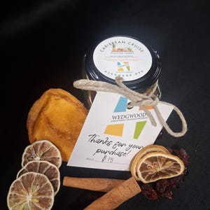 May include: A jar labeled "Caribbean Cruise Stovetop Simmer" with a tag that says "Thanks for your purchase!" is surrounded by dried fruit, cinnamon sticks, and spices. The jar is tied with twine.